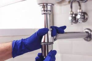 plumber working on a kitchen sink pipe with gloves on